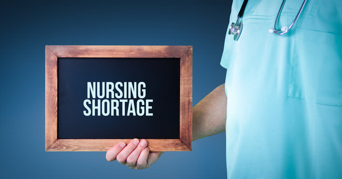 Nursing shortage. Doctor shows sign/board with wooden frame. Background blue