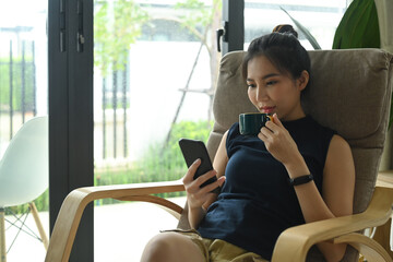 Young woman drinking coffee and checking social media news on her mobile phone.