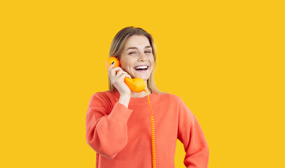 Portrait of joyful young woman talking on landline phone isolated on yellow background. Cheerful caucasian girl laughing loudly while holding orange wire retro handset. Banner. Copy space.