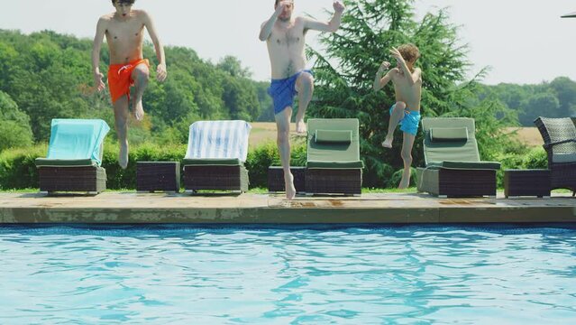 Father jumping into outdoor swimming pool on summer vacation together - shot in slow motion
