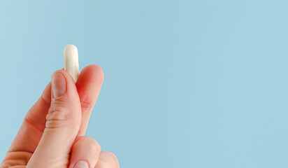 Female hand holding white capsule on blue background. Close, copy space. Pharmacology concept