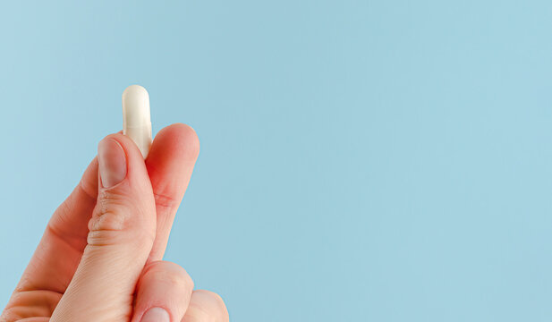 Female hand holding white capsule on blue background. Close, copy space. Pharmacology concept