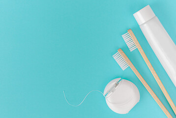 Bamboo toothbrush, toothpaste tube and dental floss on blue background. Dental care, overhead