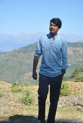 Full length front view of a young guy walking in hilly area with hand on pocket and looking away with copy space