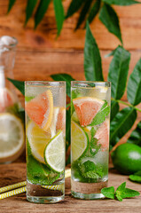 Iced citrus drink with soda, citrus fruits and mint on wooden background.