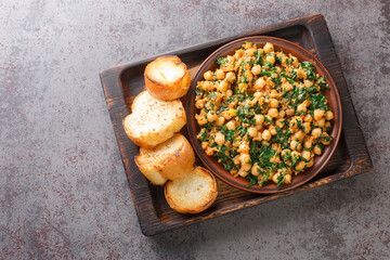 Fried spinach with chickpeas and garlic paste served with toast close-up on a wooden tray on the table. horizontal top view from above