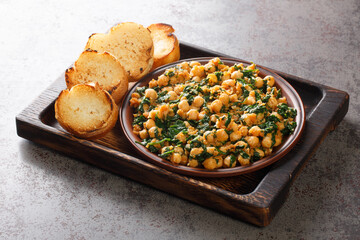 Fried spinach with chickpeas and garlic paste served with toast close-up on a wooden tray on the table. horizontal