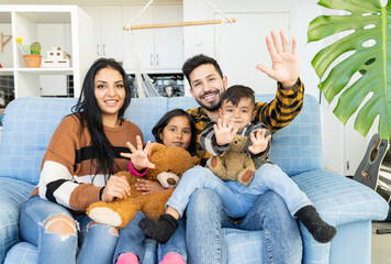 family with children on the sofa at home waving hello