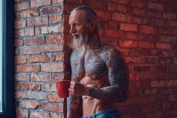 Muscular elderly man with tattooed body with coffee cup