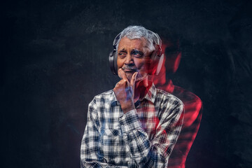 Pensive old man with headphones dressed in plaid shirt