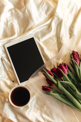 tablet, peonies and coffee on the bed 