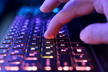 Working on a neon computer keyboard with colored backlighting. Computer video games, hacking, technology, internet concept. Selected focus.
