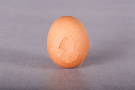 a chicken egg with a crack stands on a gray background
