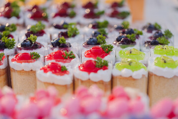 Cute cupcakes lined up in a row topped with jam and fruit, blueberries, strawberries, cherries and kiwi, Selective focus, Concept of Bakery shop, baking school, freelance, personal or small business.