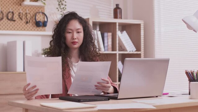 At home, an Asian designer works on a desk with a laptop, searching for jobs and paperwork.Designer web development website template design user ui application on paper.
