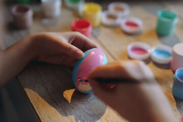close up view of child hands colouring easer egg with gouache paint