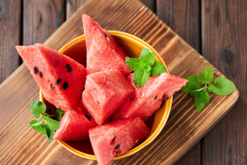 Sliced watermelon decorated with mint leaves on brown wooden background. Close-up, selective focus