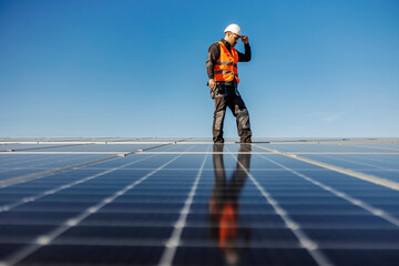 A worker walking around roof and checking on screws on solar panels.