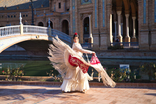 Flamenco dancer, woman, brunette and beautiful typical spanish dancer is dancing with a red manila shawl in a square in seville. Flamenco concept of cultural heritage of humanity.
