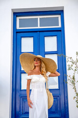 A beautiful tourist wearing straw hat standing over blue door at the balcony
