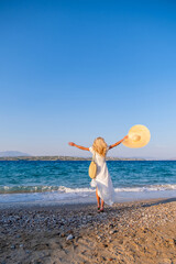 attractive young woman wearing dress standing at sea shore with hands raised