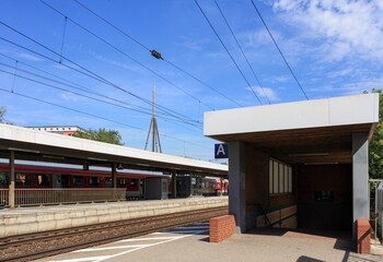 View of platform and train track at train station in summer with clouds in blue sky background. No people.