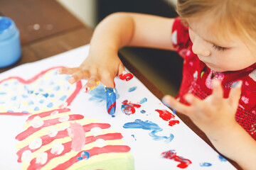 Obraz na płótnie Canvas Little creative toddler girl painting with finger colors a fish. Active child having fun with drawing at home, in kindergaten or preschool. Education and distance learning for kids. Creaitve activity.