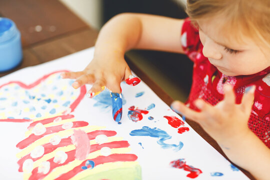 Little creative toddler girl painting with finger colors a fish. Active child having fun with drawing at home, in kindergaten or preschool. Education and distance learning for kids. Creaitve activity.