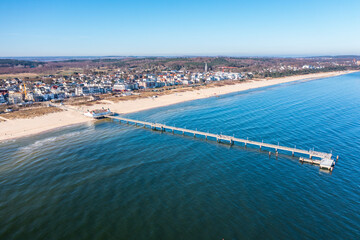 Aerial view of the coastline around city of Ahlbeck on the peninsula Usedom in Germany during a sunny day in early spring. Pier juts out into the Baltic Sea. The famous building are behind the beach. - obrazy, fototapety, plakaty