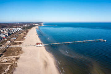 Aerial view of the coastline around city of Ahlbeck on the peninsula Usedom in Germany during a sunny day in early spring. Pier juts out into the Baltic Sea. The famous building are behind the beach.