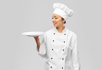 cooking, culinary and people concept - happy smiling female chef holding empty plate over grey background