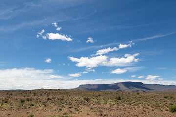A view of the wide, open and arid Karoo with mountains in the distance and blue sky with white clouds