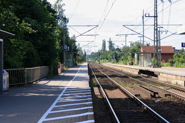 Perspective view of train tracks and platform at train station in summer with clouds in sunny blue sky background. No people.