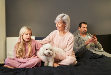 mother and daughter playing with the dog and the father looking at the cell phone