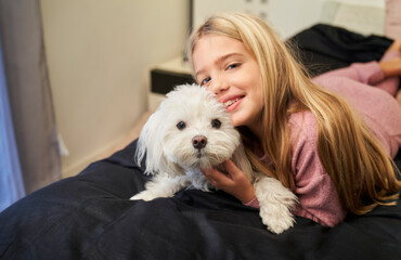 blonde girl lying in bed with her smiling dog looking at the camera