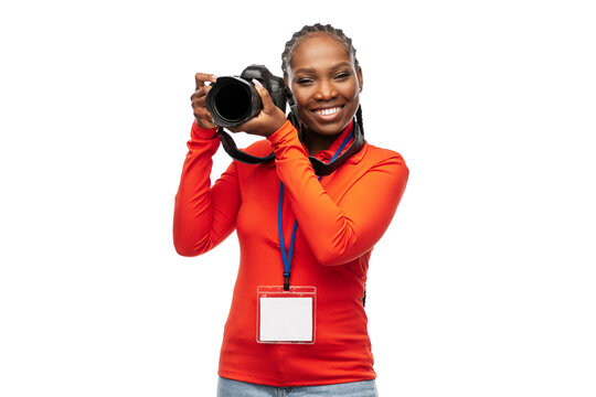 people, profession and photography concept - happy young woman or press photographer with digital camera and conference id card photographing over white background