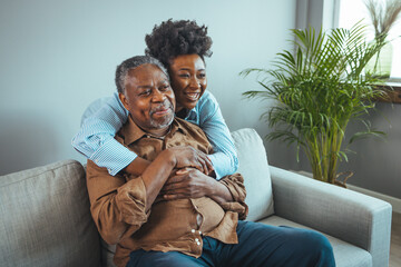 Loving senior man embracing his daughter while sitting on sofa smiling. An attractive young woman...