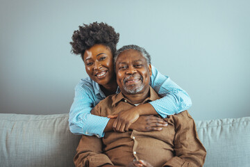Loving senior man embracing his daughter while sitting on sofa smiling. An attractive young woman...