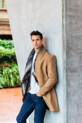 Obraz premium Portrait of stylish handsome young man standing outdoors and leaning on wall. Man wearing jacket and scarf