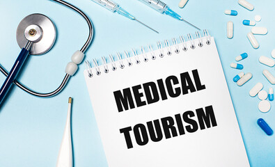 An electronic thermometer, a stethoscope, pills, syringes and a notebook with the text MEDICAL TOURISM