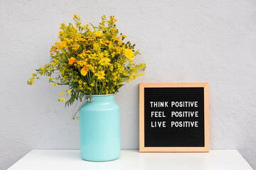 Think positive, feel positive, live positive. Motivational quote on letter board and bouquet yellow flowers on white table against grey stone wall. Concept inspirational quote of the day