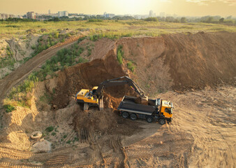Earthmoving at construction site. Excavator load soil in dump truck. Excavator on earthworks. Open...