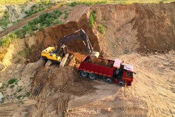Earthmoving at construction site. Excavator load soil in dump truck. Excavator on earthworks. Open pit development and sand mining. Loader digg ground for foundation pit. Earthmover and digger..