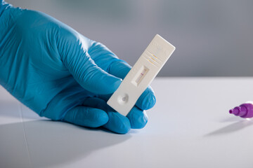 Close-up of hand in medical gloves handling showing result of  antigen self test or quick test for Corona or Covid-19 detection