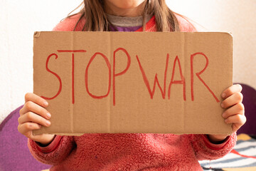 A little girl holds a poster with the words stop the war at her home in Ukraine and asks to stop...