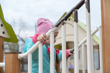 Portrait of a preschool child on the playground. A five-year-old girl in a pink hat walks up and down the stairs holding onto the railing. Childhood. View from the bottom up.