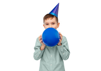 birthday, childhood and people concept - portrait of little boy in dress and party hat blowing balloon over white background