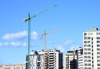 Fototapeta na wymiar Tower crane against the blue sky. Tower crane on the construction of a residential building in Spain. Construction site with cranes for building construction. Сranes in action. Housing renovation 