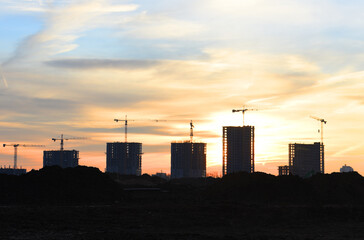 Fototapeta na wymiar Panorama of construction cranes during the construction of a residential building at sunset. Construction site at sunset with a tower crane and unfinished buildings and residential houses skyscrapers.