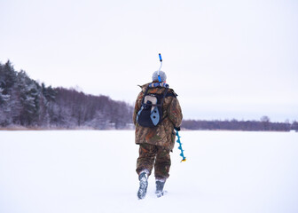 Ice fishing on frozen lake. Fishermen in camouflage clothing is walking on frozen lake for ice fishing. Fisherman on lake with drill for drilling holes in the ice for catching fish. Winter fishing.